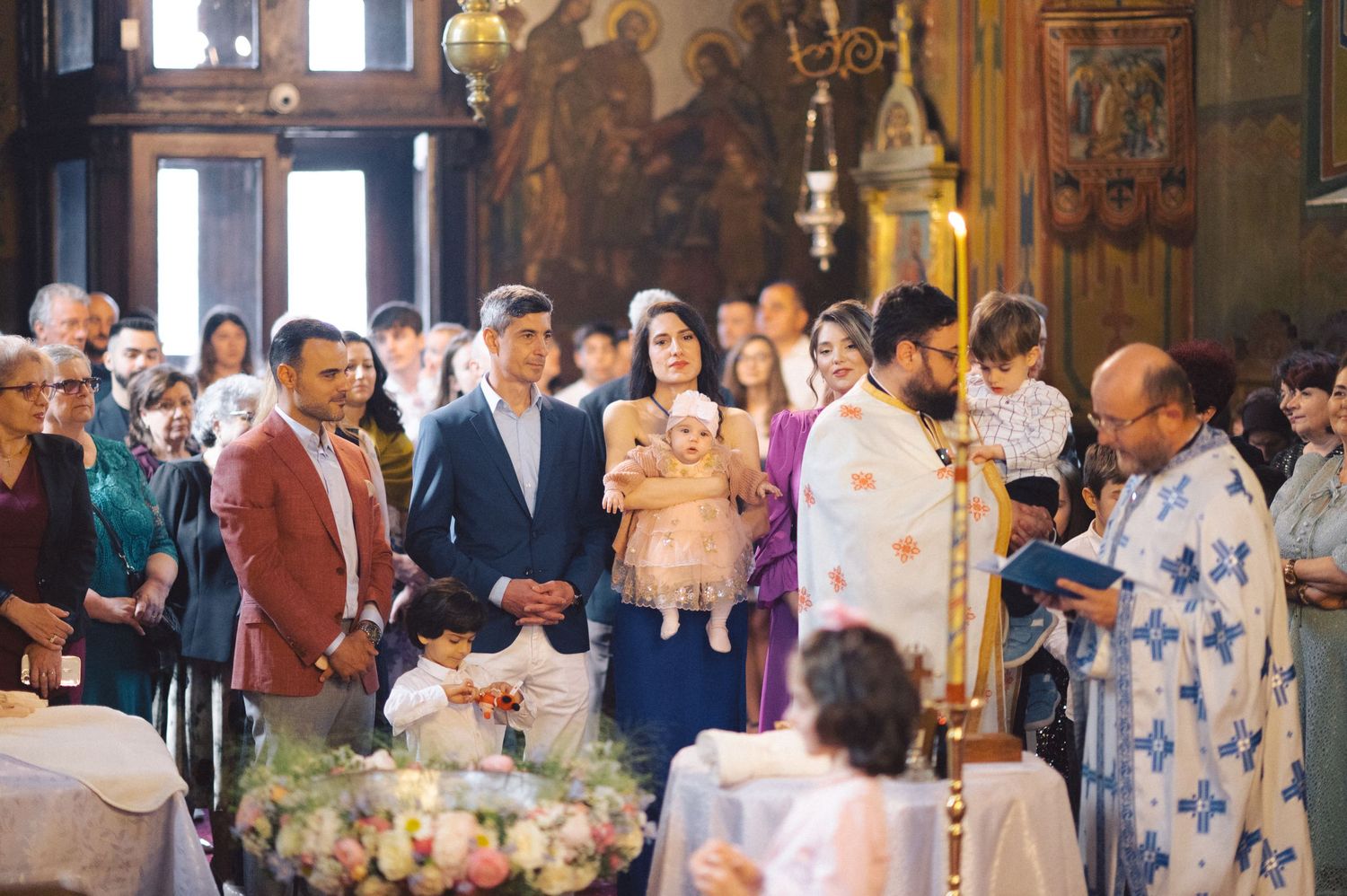 A traditional Orthodox Christian baptismal ceremony taking place inside an ornate church with gathered attendees.