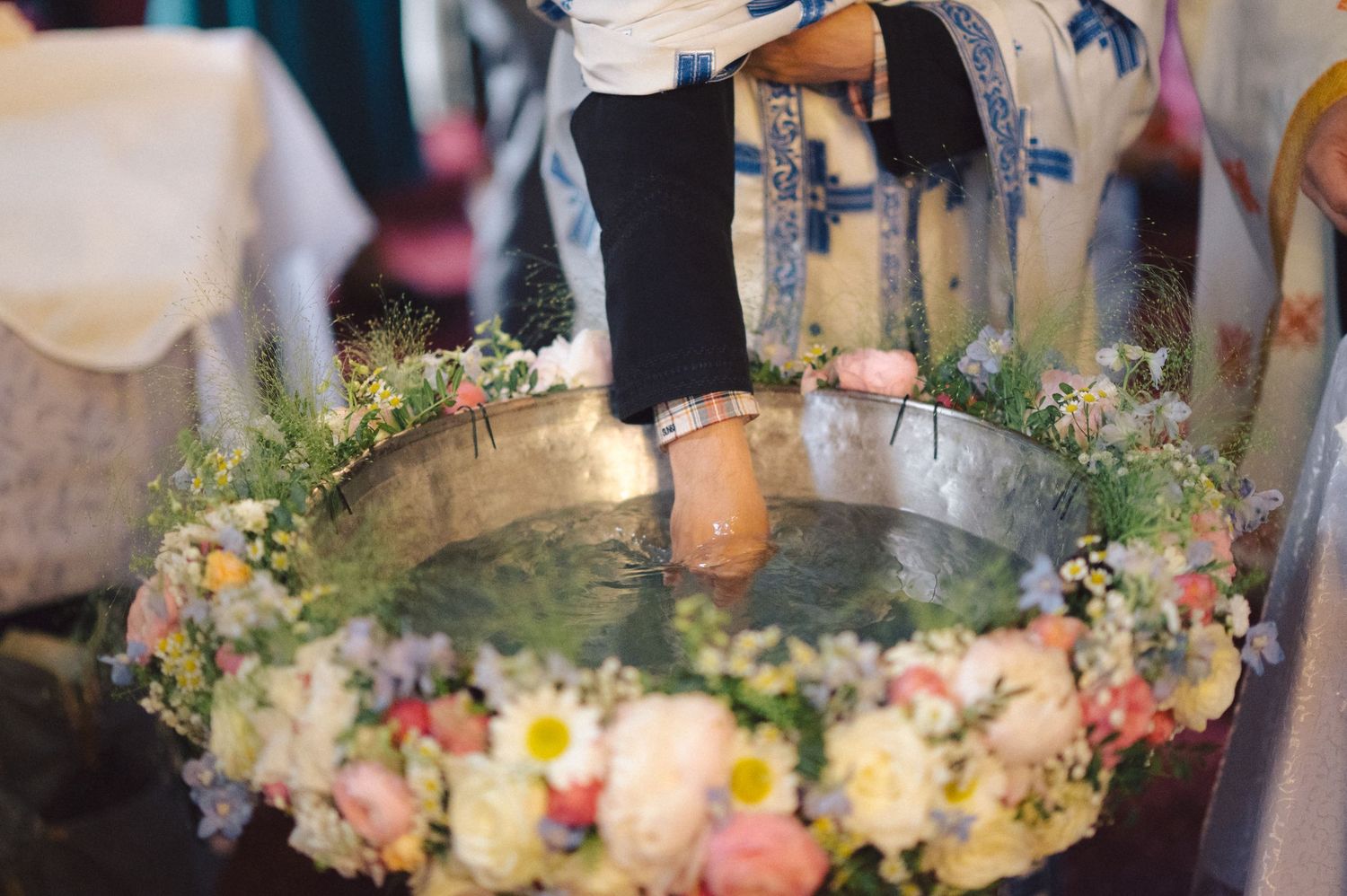 A decorated baptismal font adorned with a floral wreath of pink and yellow flowers floating on holy water.
