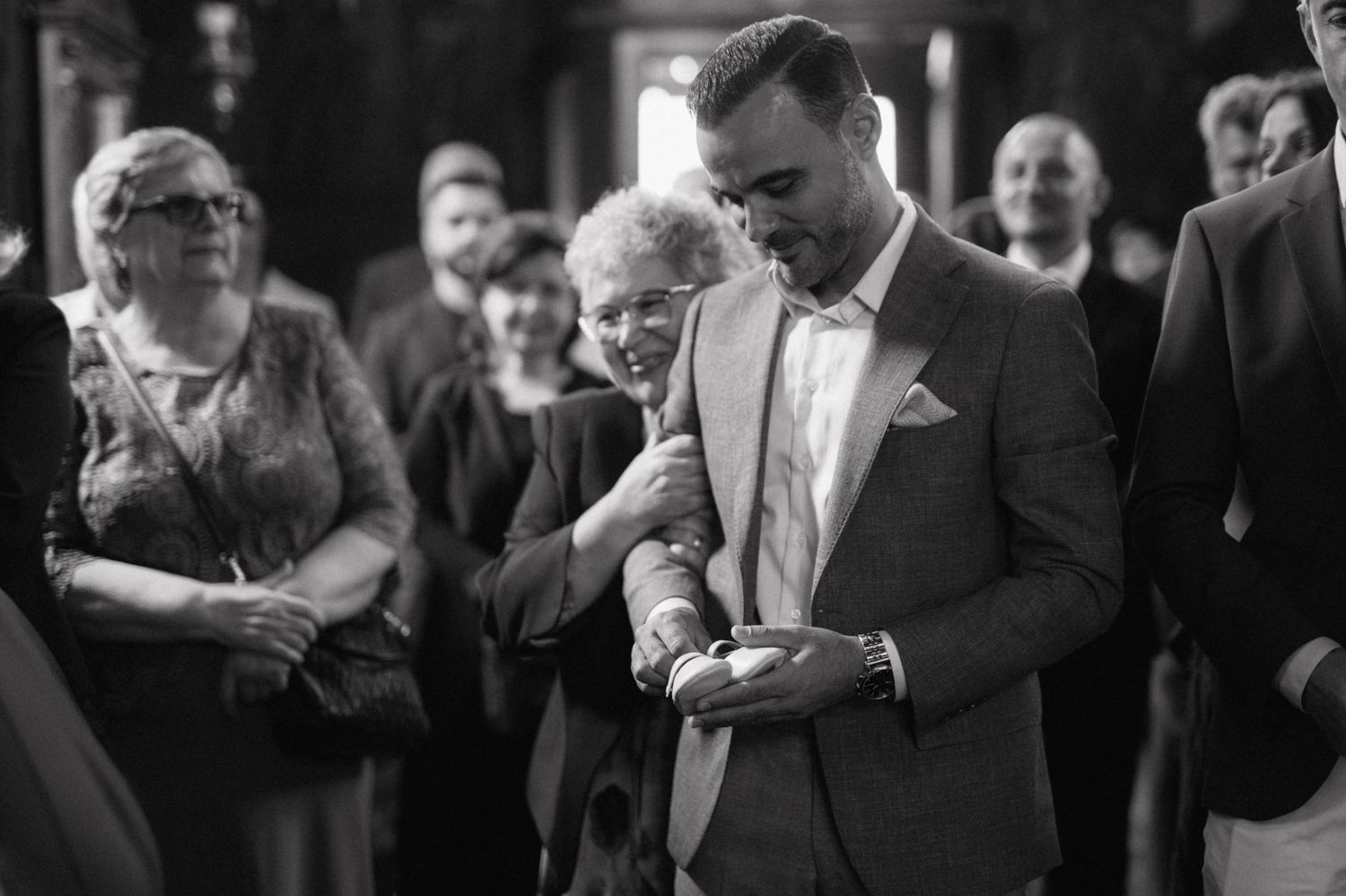 A black and white photo of a christening ceremony with attendees watching the proceedings.