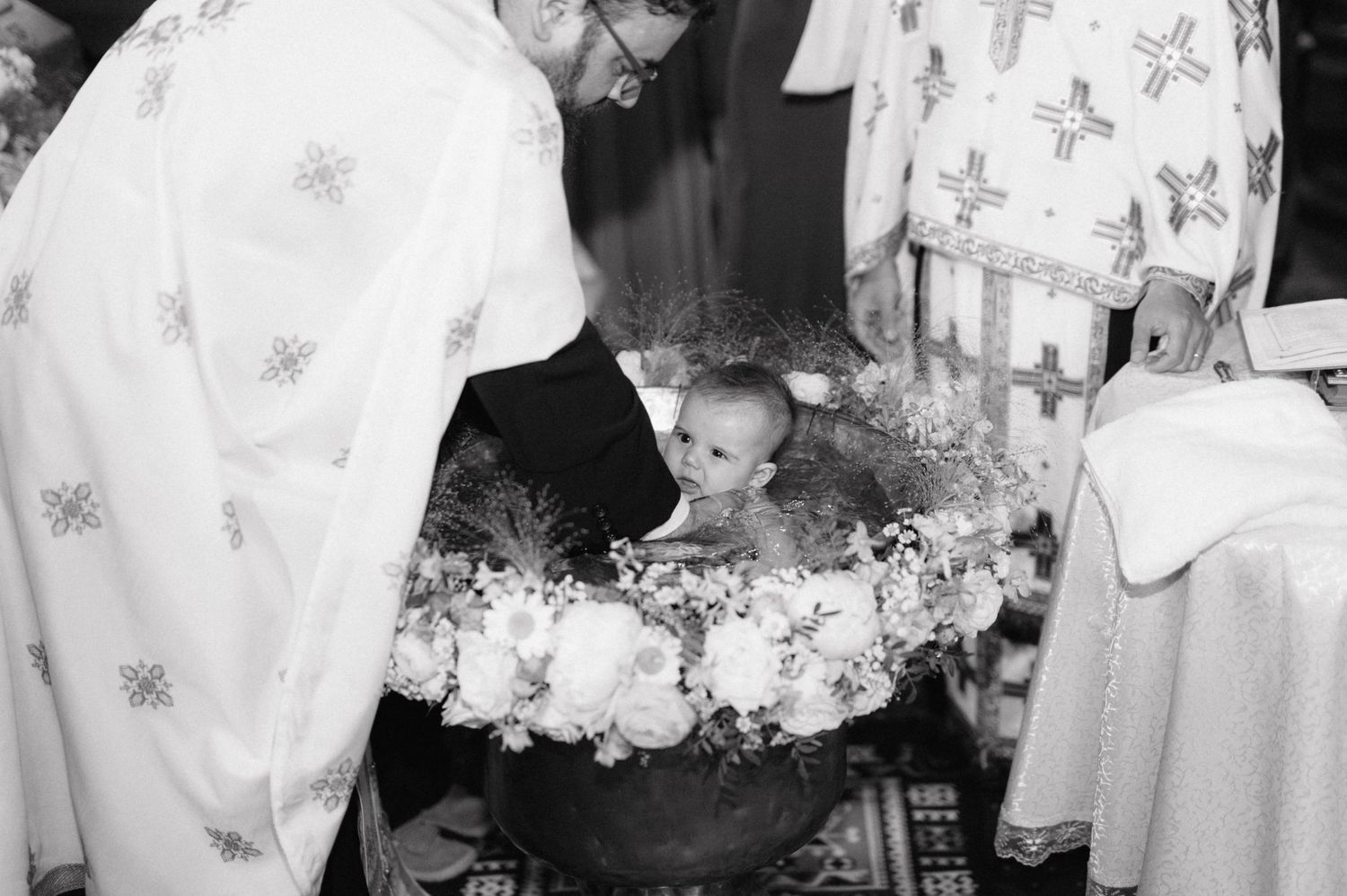 Black and white photograph shows a baby being baptized in an ornate church setting.