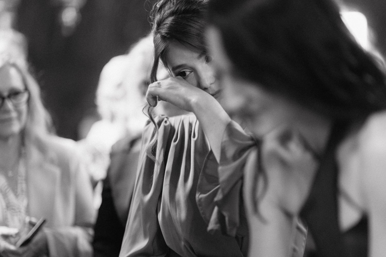 Black and white photo showing an emotional person pressing cloth to their face in the midst of others at an event.