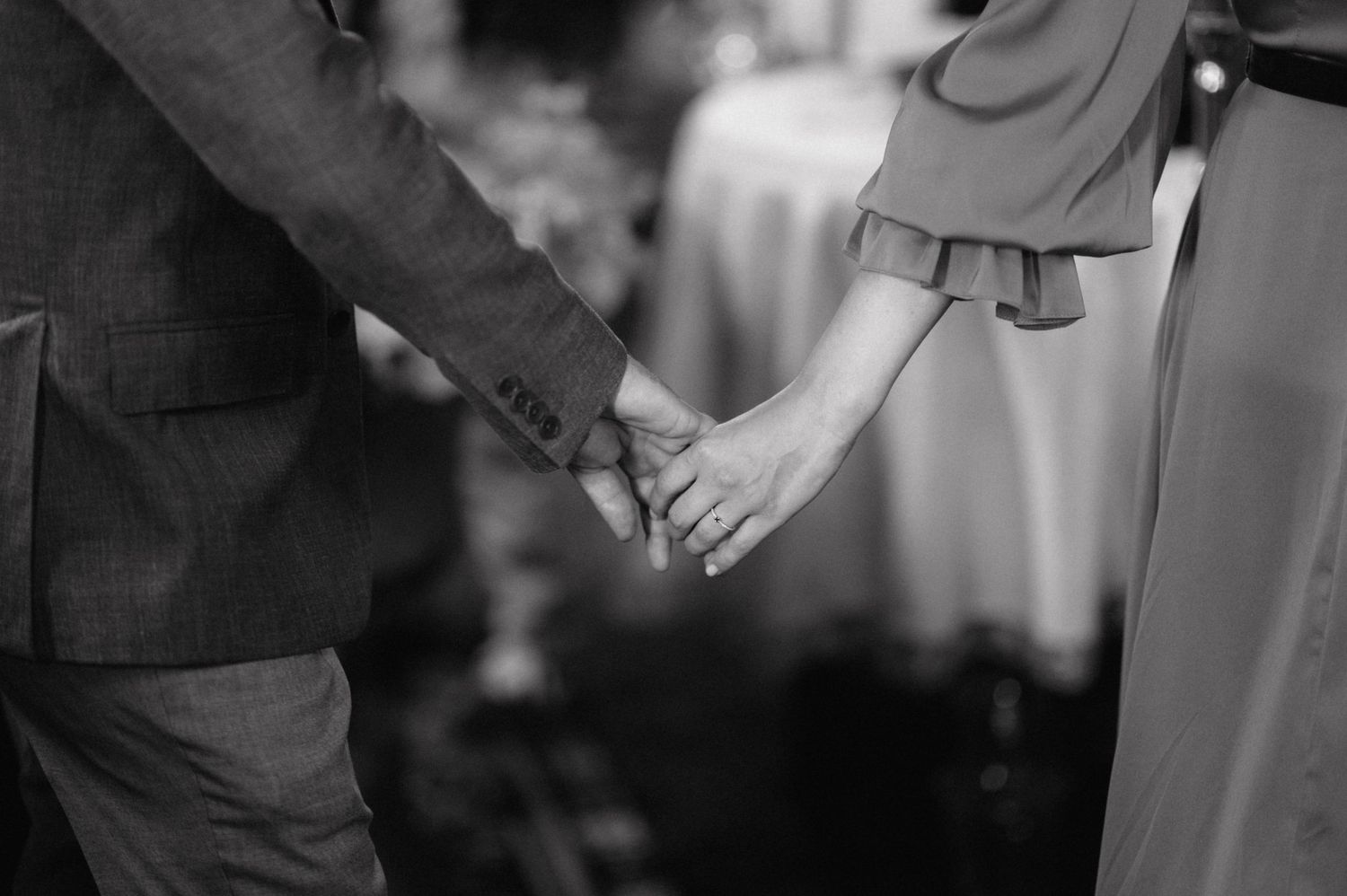 A black and white closeup of two people holding hands during what appears to be a formal event.