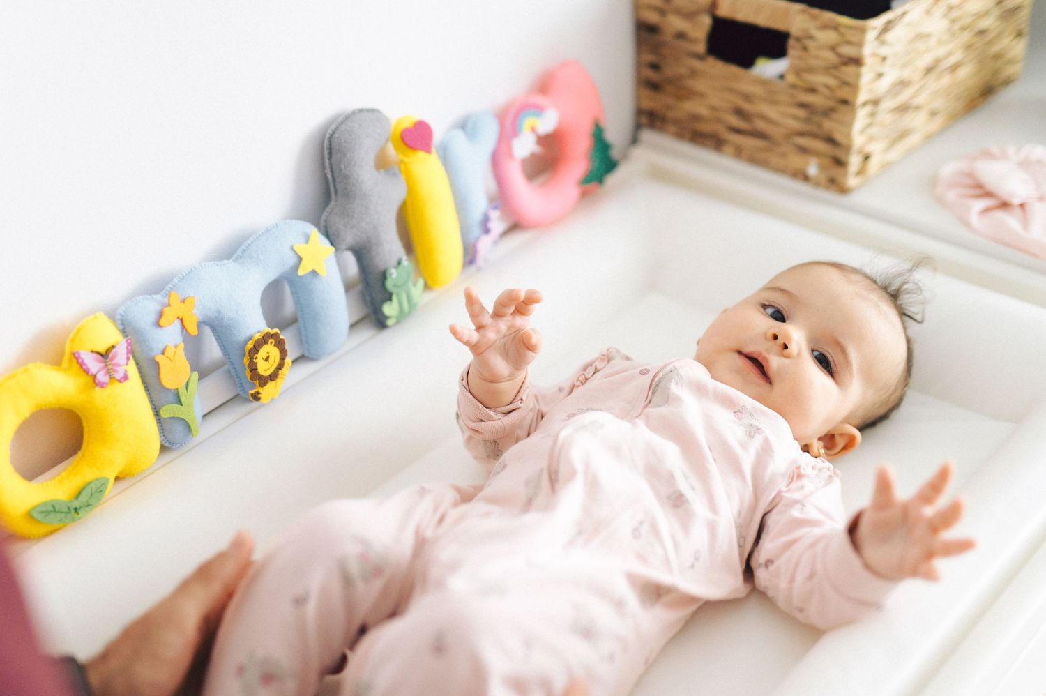 Baby in pink onesie lies on changing table near colorful plush caterpillar toy.