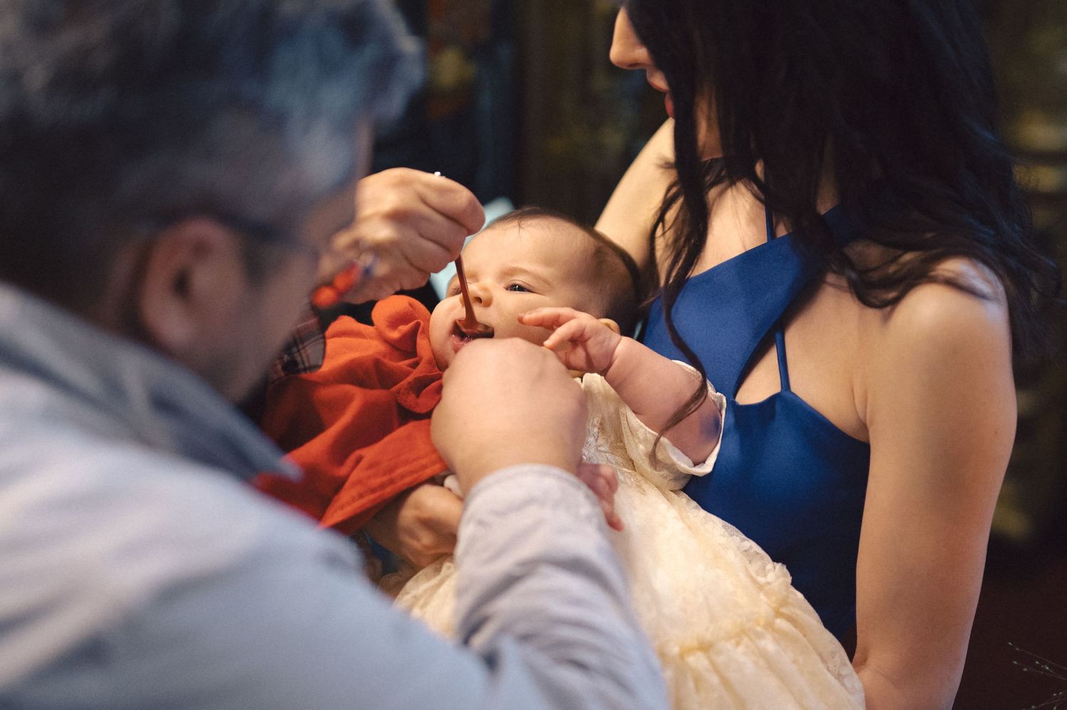 A baby in an orange outfit being held during what appears to be a special ceremony or gathering.