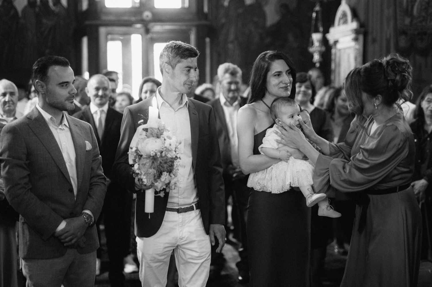 Black and white photo showing a joyful baptism ceremony gathering inside a church with guests celebrating the occasion.