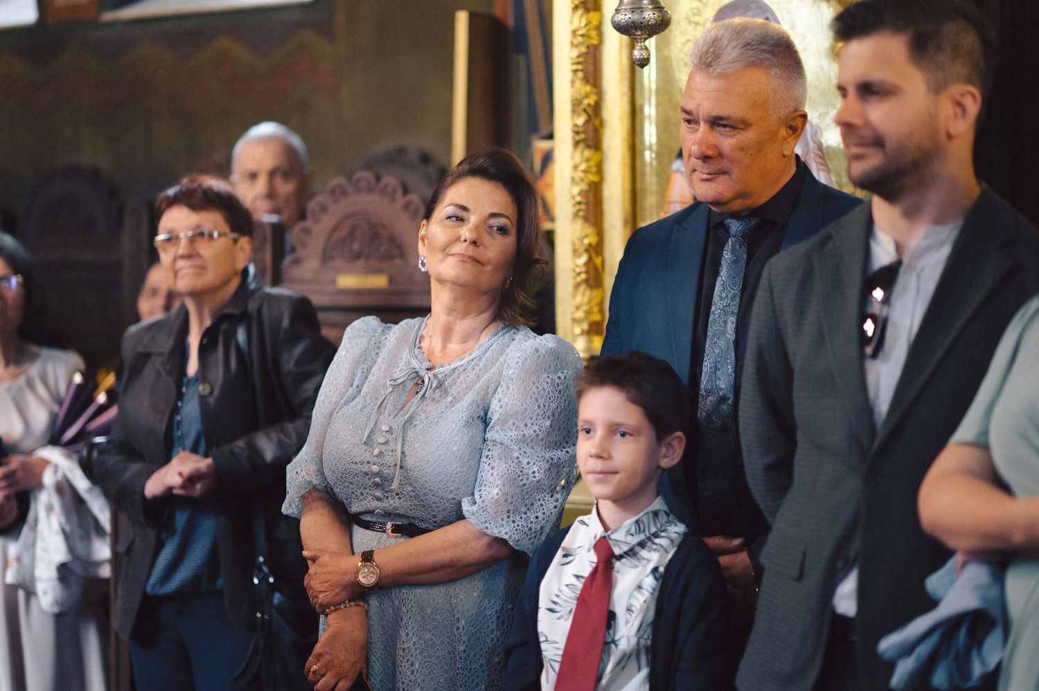 A group of well-dressed people in formal attire gather together at an elegant event with ornate golden decor.
