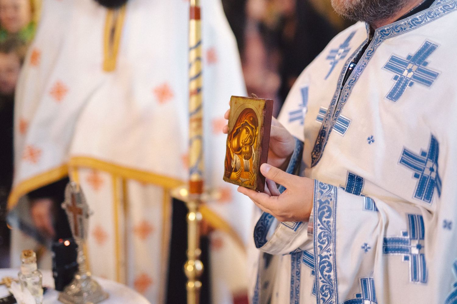 Orthodox priest in traditional blue and white vestments holding a religious icon during church service.