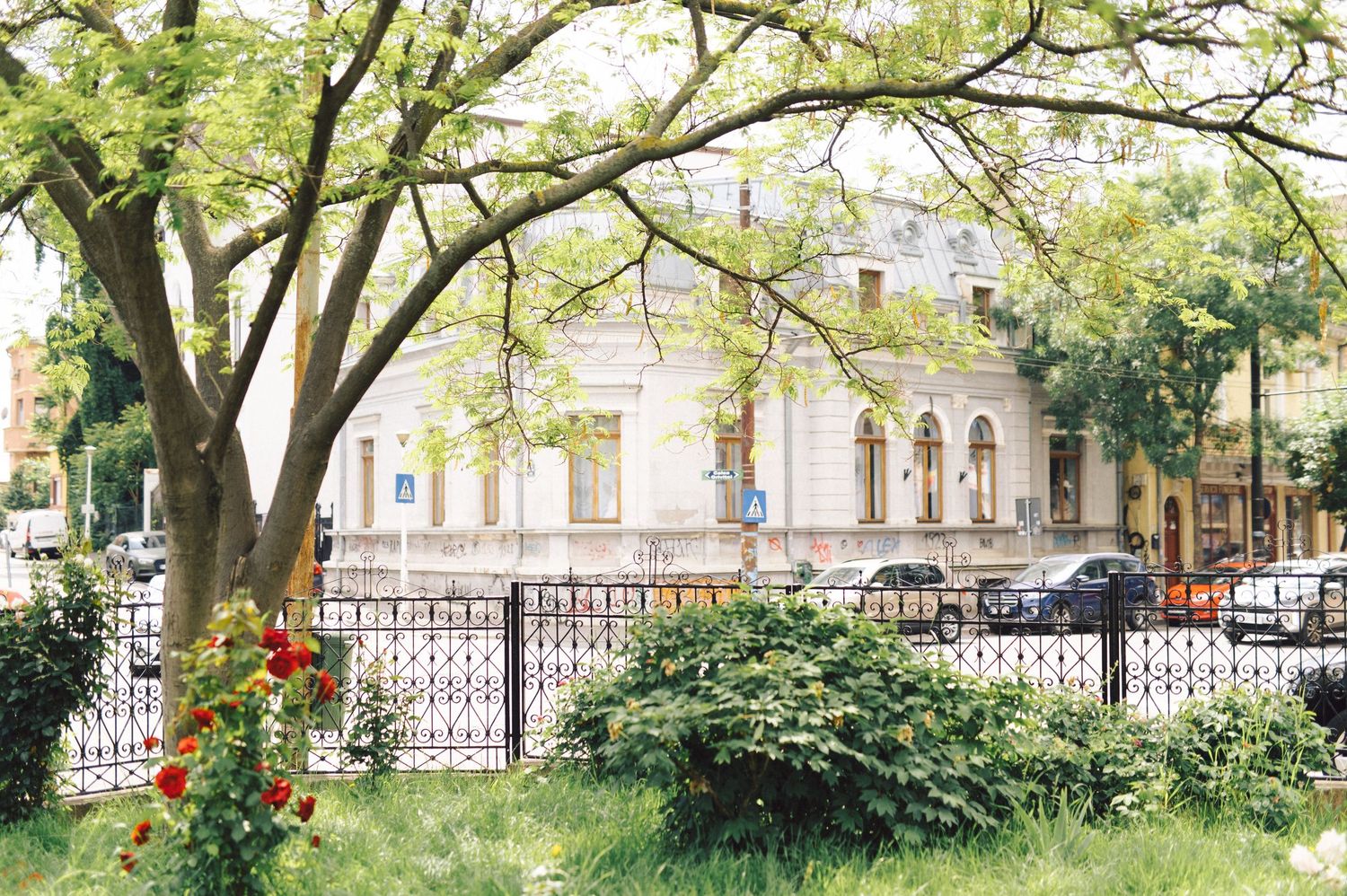 A grand white historic building with ornate architecture surrounded by lush green trees and an iron fence.