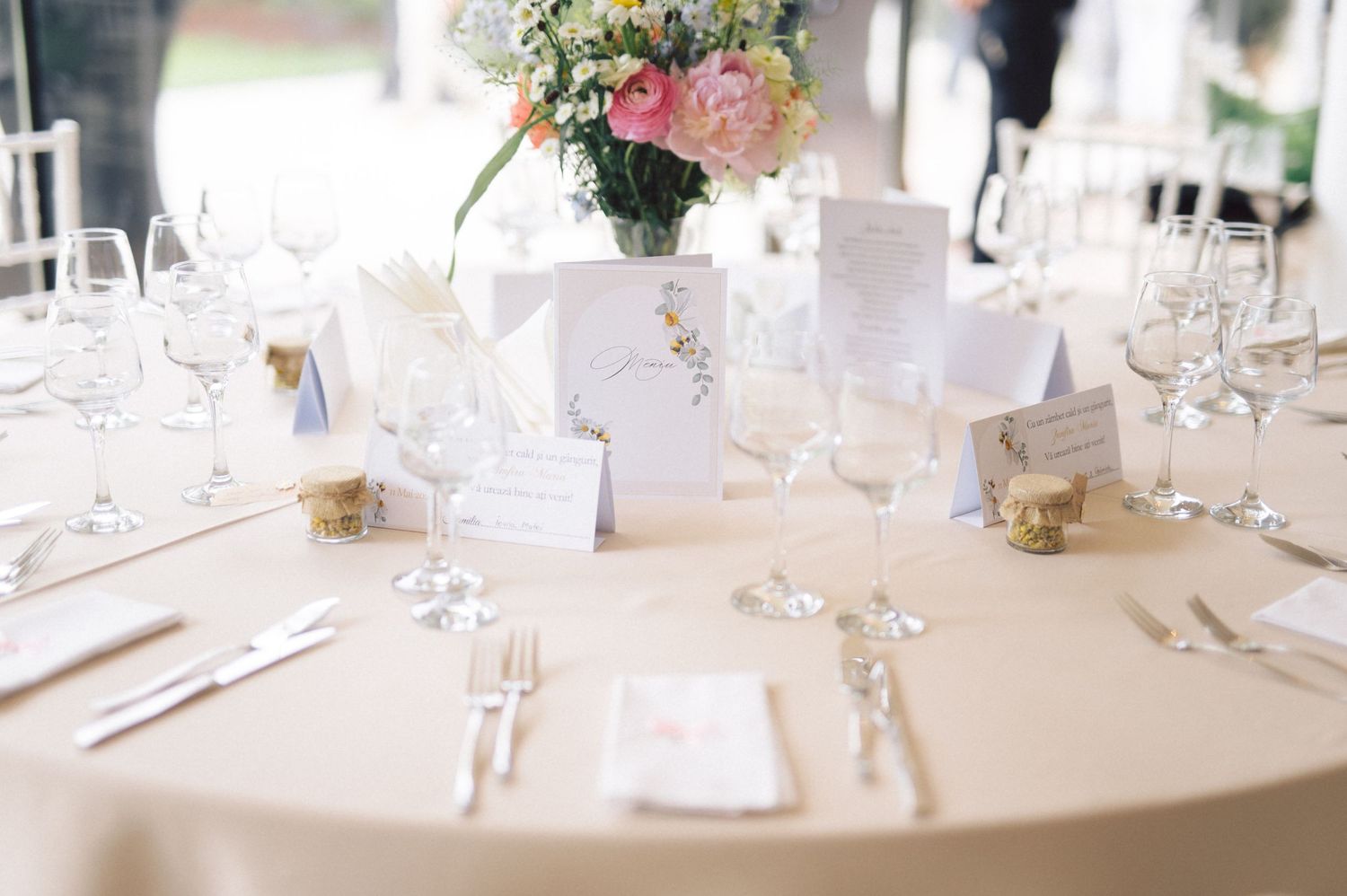 An elegant wedding reception table setting with a pink floral centerpiece, white linens, and crystal glassware.