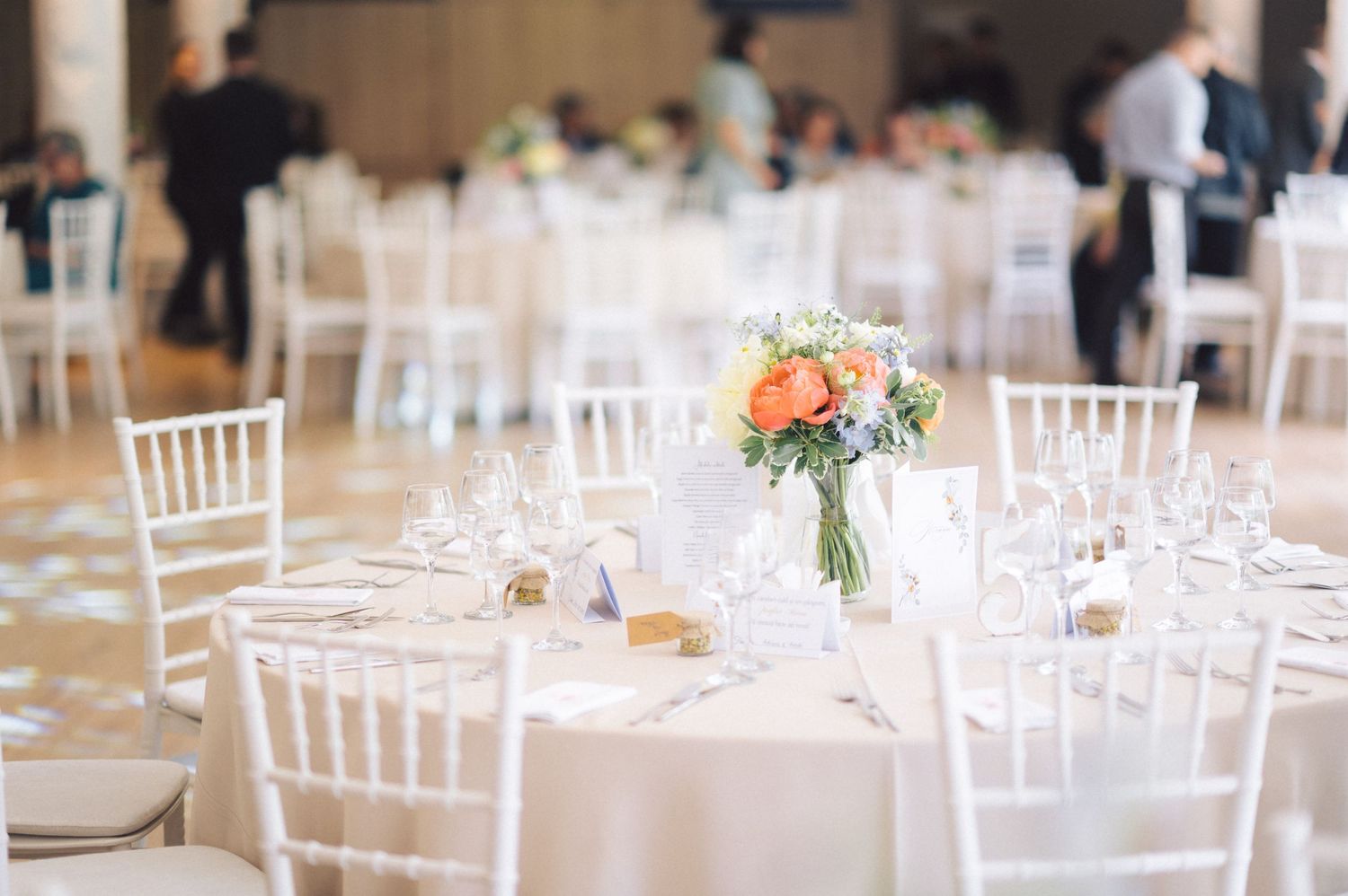 White chiavari chairs surround round reception tables decorated with floral centerpieces in a bright banquet hall.