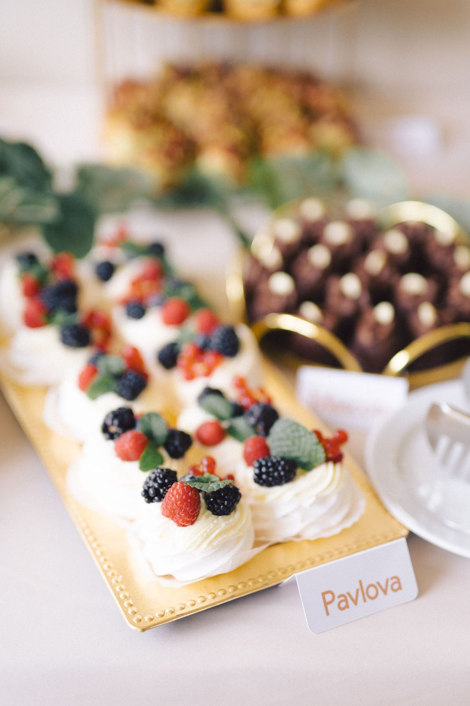 A delicate Pavlova dessert topped with fresh berries and whipped cream sits on a golden serving platter at a dessert table.