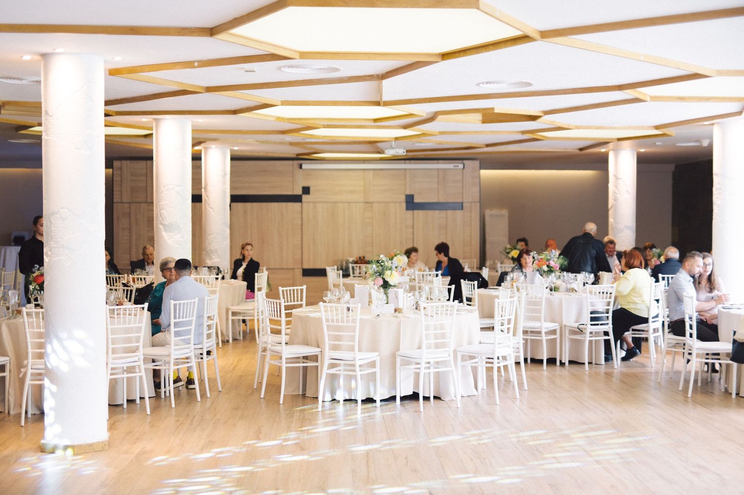 Reception venue with white chairs and tables set up for a wedding celebration under modern lighting.