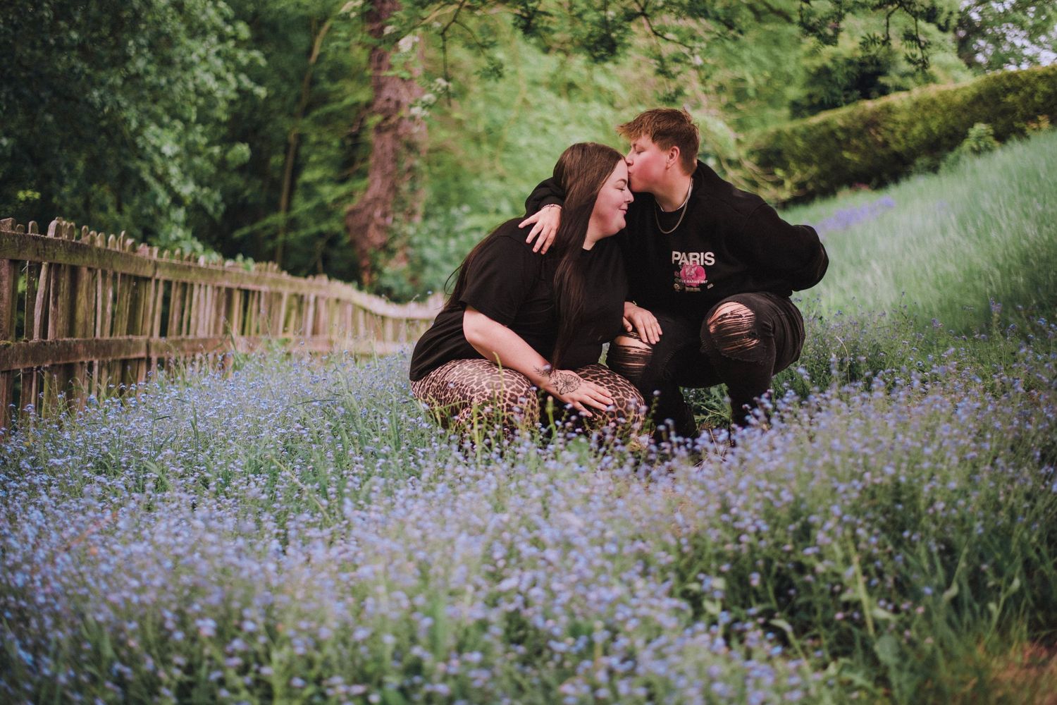 A couple sits together surrounded by beautiful purple wildflowers in a meadow on a spring afternoon.