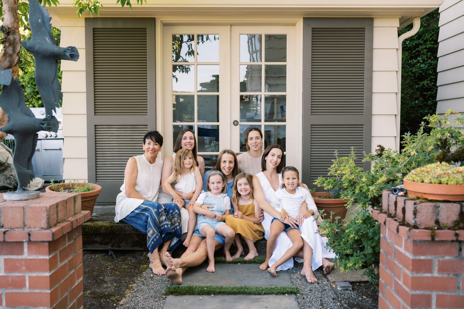Diverse group of adults and children wearing coordinated blue and neutral outfits pose together on green lawn by building.