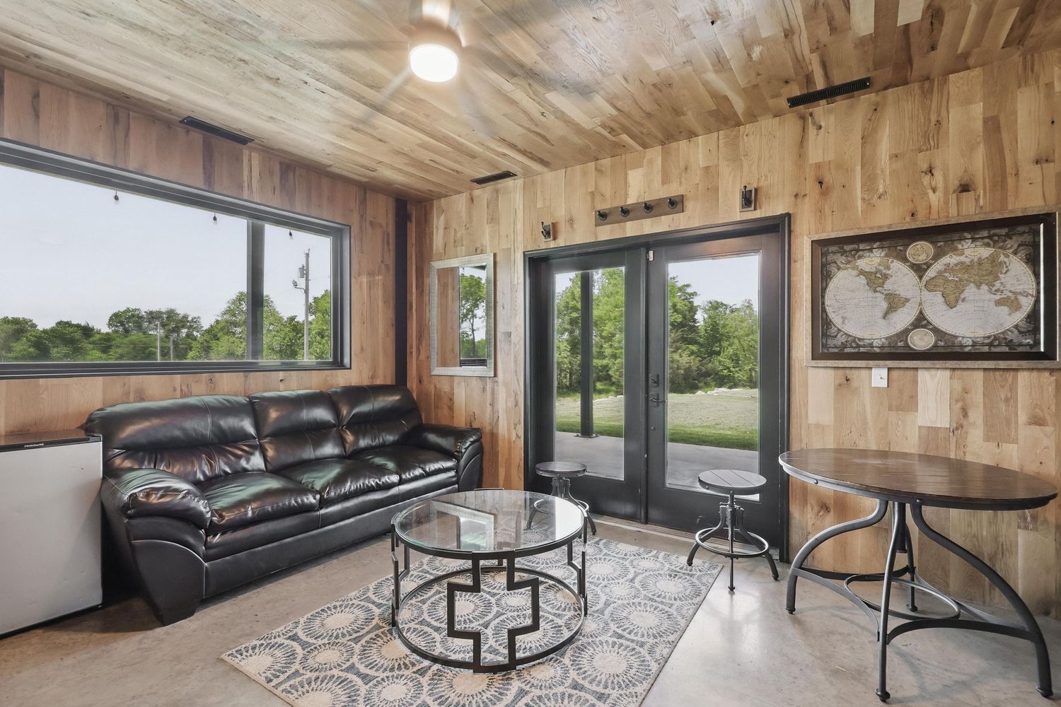 Modern living room with wood paneled walls, leather couch, round glass coffee table and windows showcasing outdoor views.