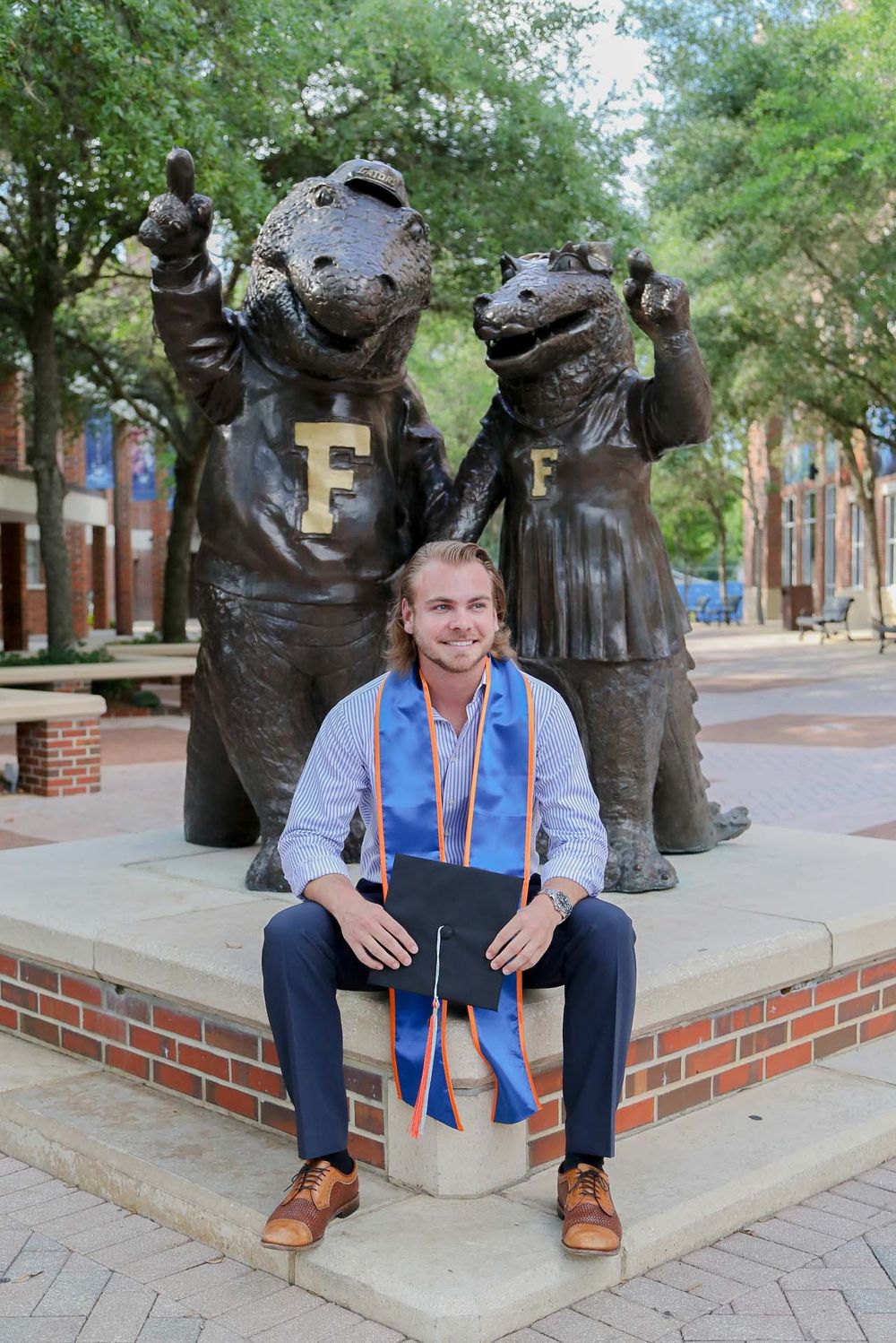 Graduate poses in front of bronze Gator mascot statues at University of Florida campus in Gainesville.