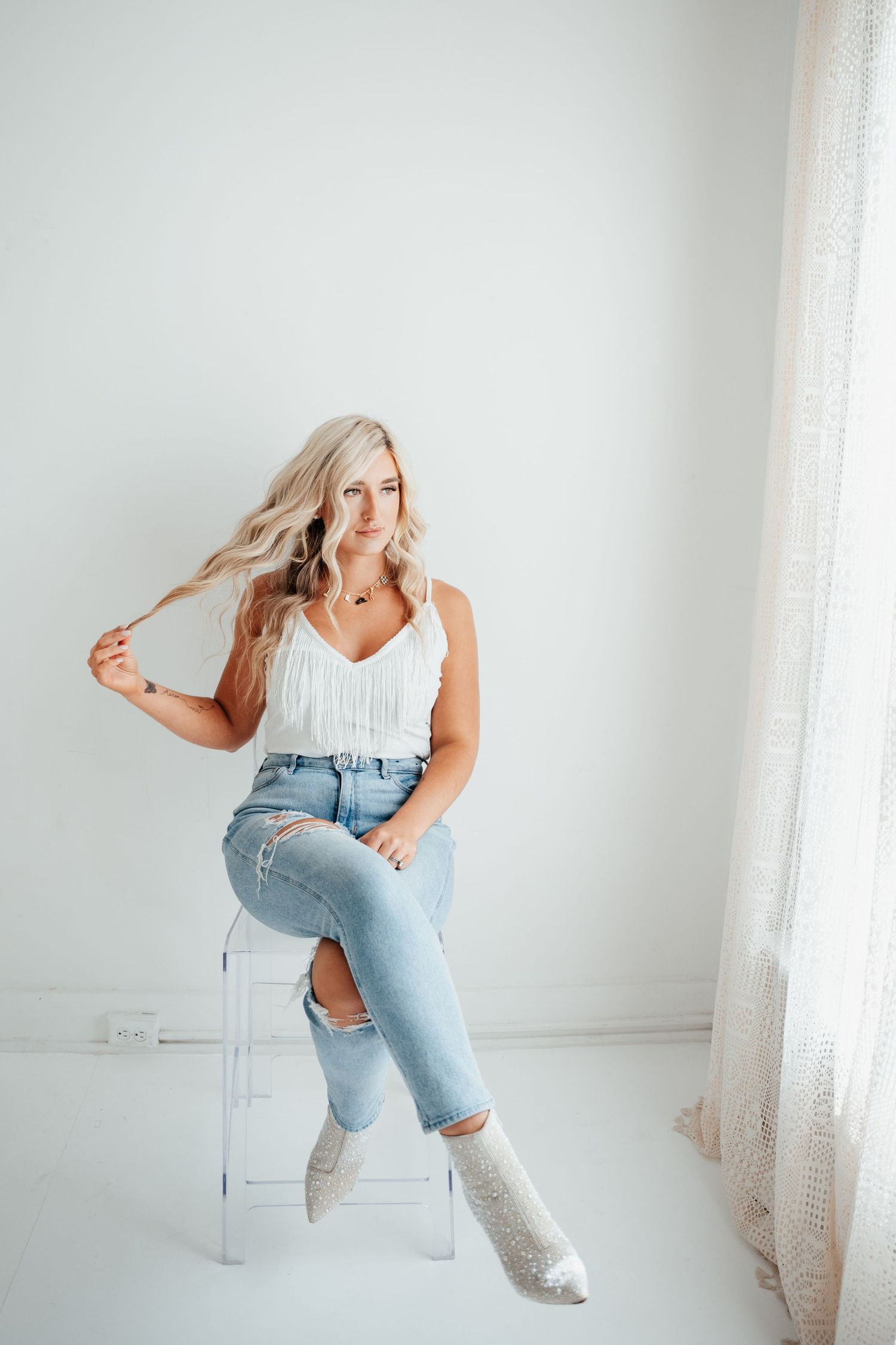 A couple poses in a bright white room with chandeliers and rustic wooden floors.