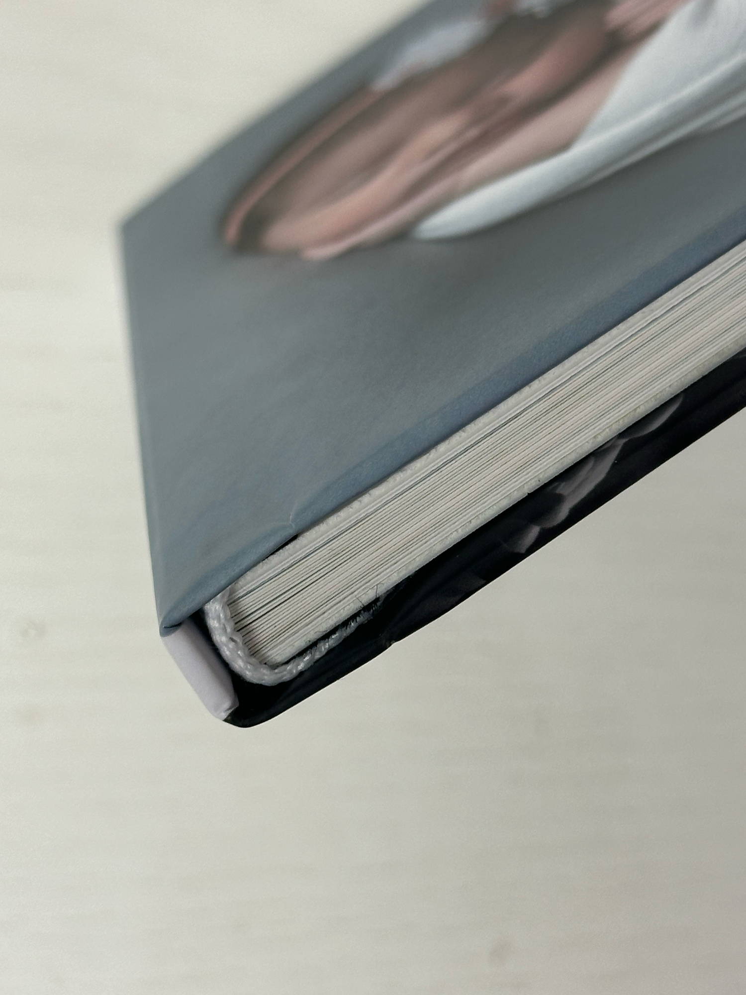 Close-up of a hardcover book spine showing pages and gray cover with a partial portrait image. Photo book