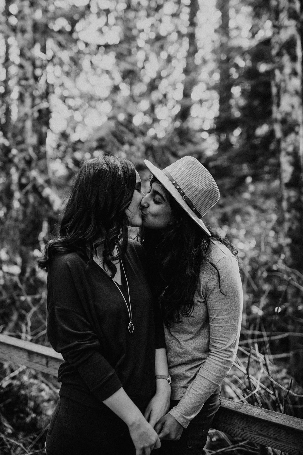 Black and white photo of two people sharing an intimate moment outdoors in a forest setting.