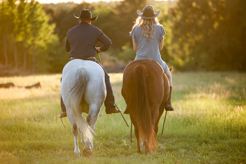 cowboy and cowgirl riding away bareback in a backlit field at sunset, golden hour, western couple,