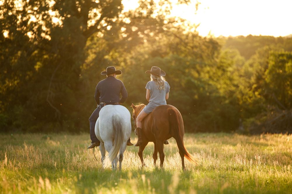 man and women riding horses through a field at sunset
