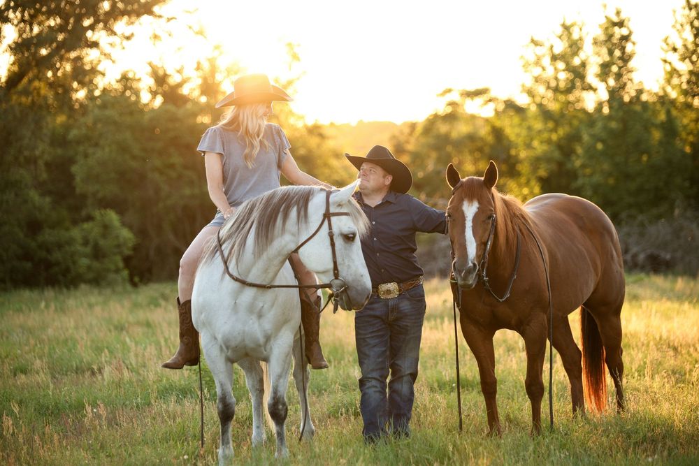 cowgirl sitting bareback with husband standing on the ground holding another horse staring up at her