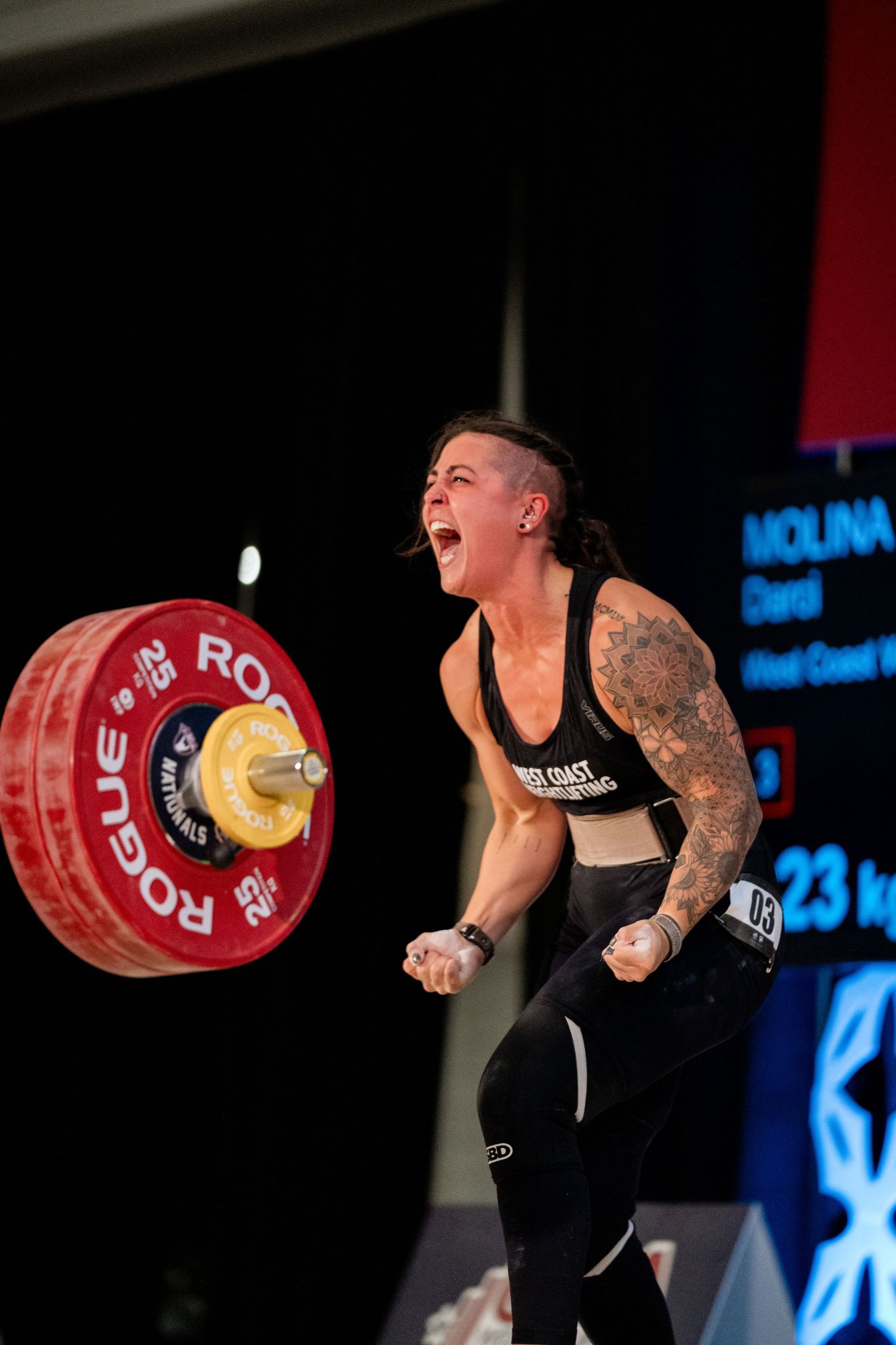 Athlete celebrates during Olympic weightlifting competition with Rogue barbell overhead.
