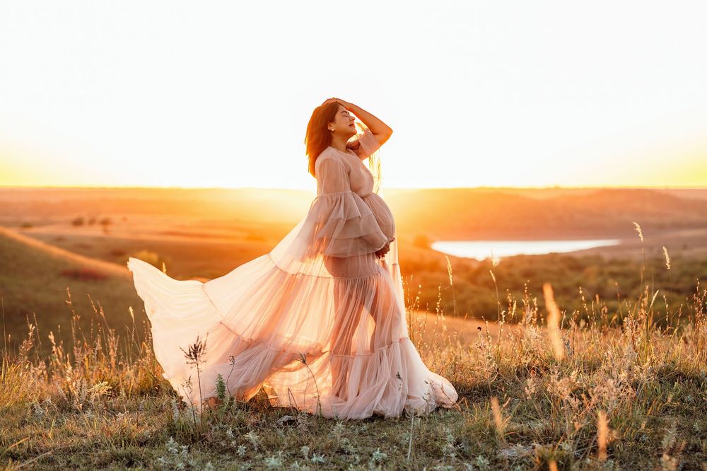 A figure in a flowing white dress twirls gracefully in a golden sunlit field during sunset.