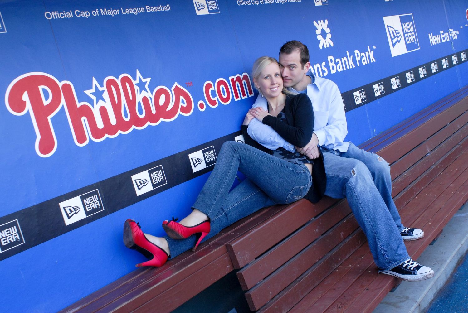 A couple poses playfully in the Phillies dugout for engagement photos.