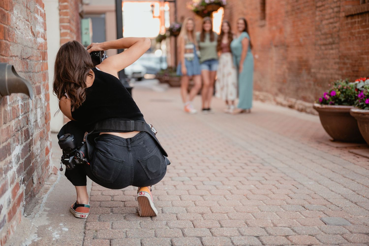 Photographer crouching on brick sidewalk capturing photos of subjects in the distance.