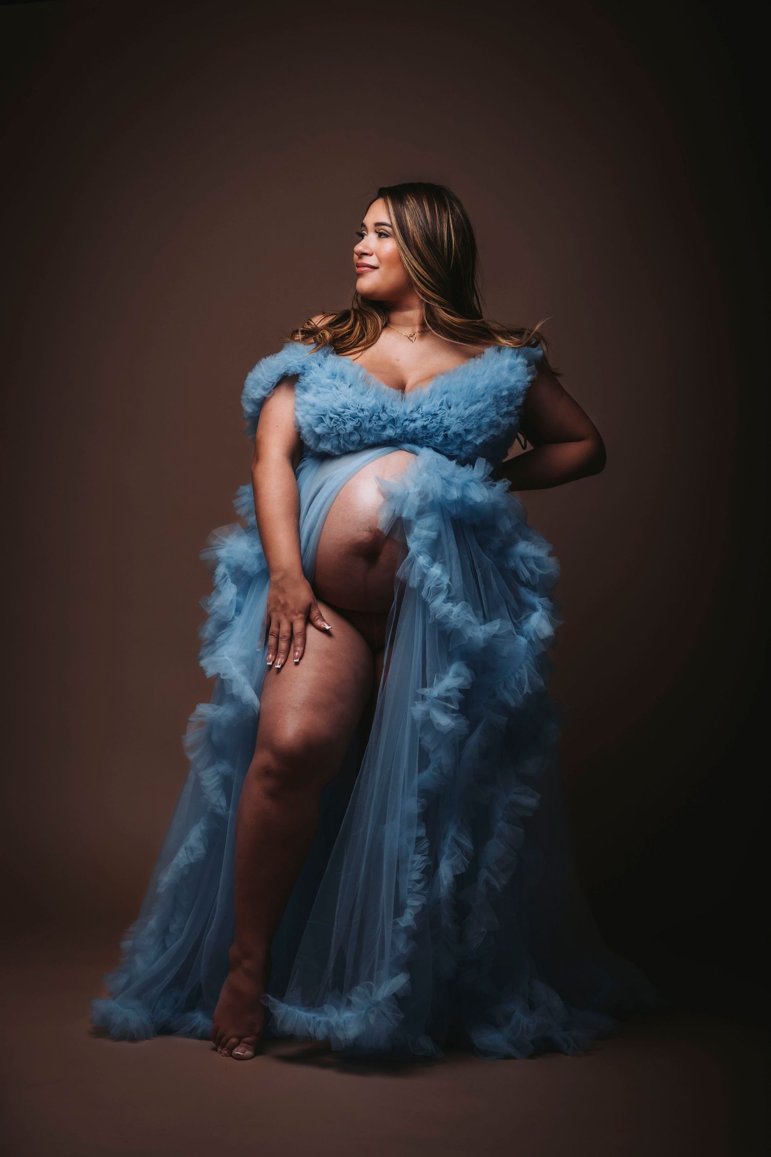 A maternity photo featuring an ethereal powder blue tulle gown against a dark background.