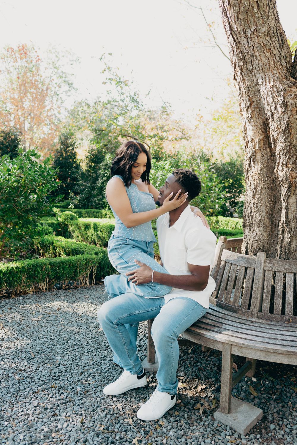 A couple shares an intimate moment while sitting together on a wooden bench in a peaceful garden setting. Dallas Engagement session