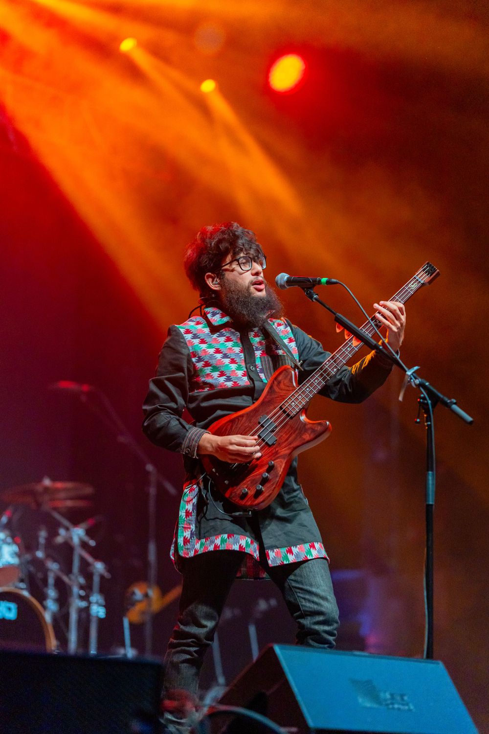 A musician performs with a bass guitar under dramatic red stage lighting.