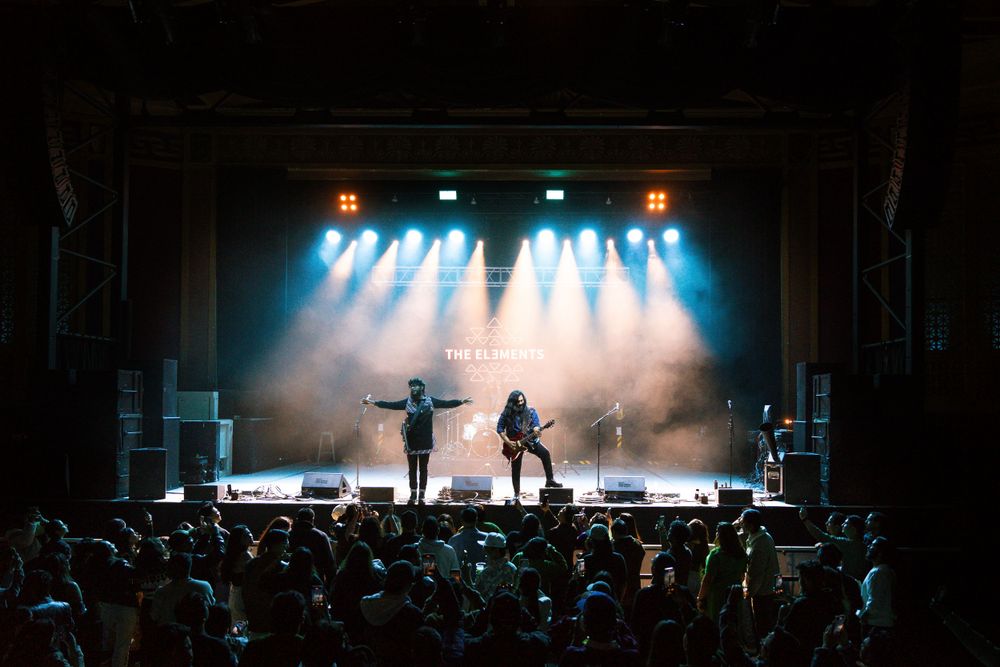 Silhouetted performers on stage with dramatic backlighting and crowd visible below.