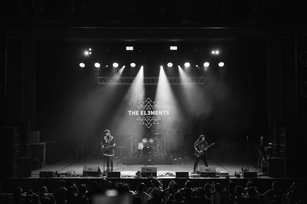 Black and white concert photo showing band performing under dramatic stage lighting.