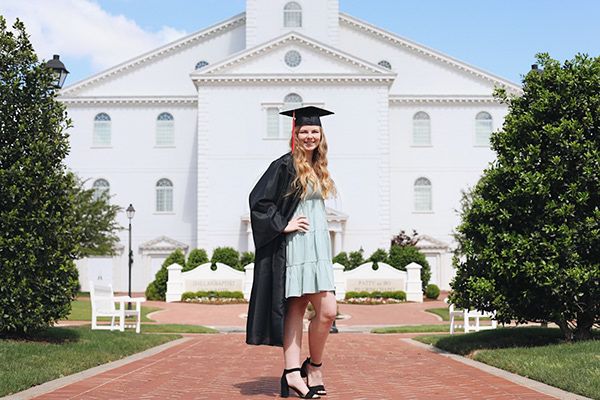 Girl in front of building with graduation gown.