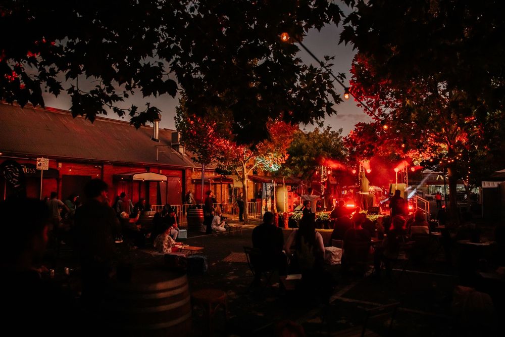 Night market scene illuminated by red lights with silhouettes of people and trees.