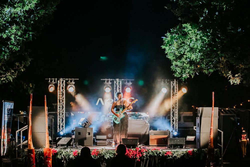 Music festival stage with atmospheric lighting and smoke effects surrounded by trees at night.