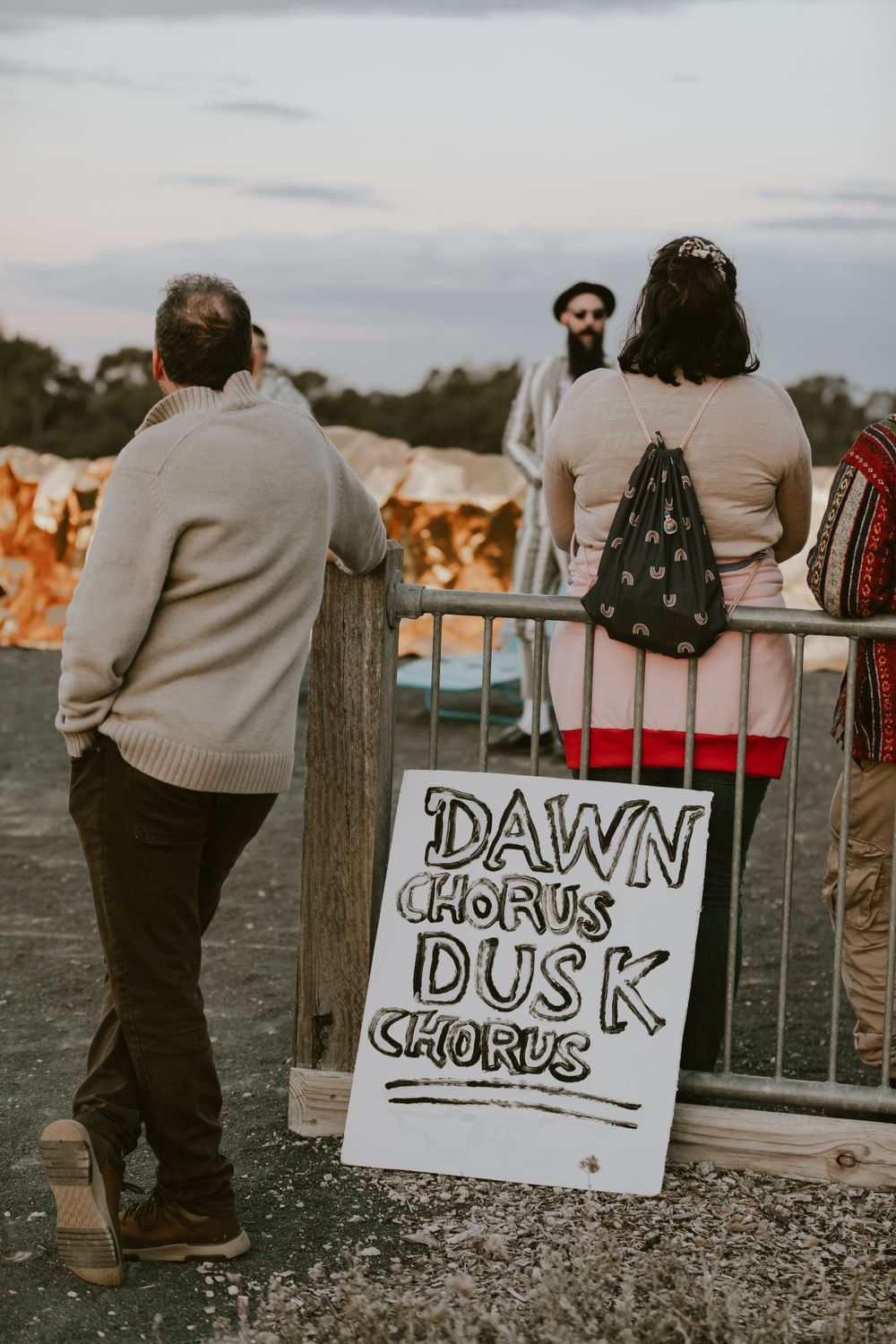 Event sign reading 'Dawn Chorus Dusk' with people viewing sunset in background.