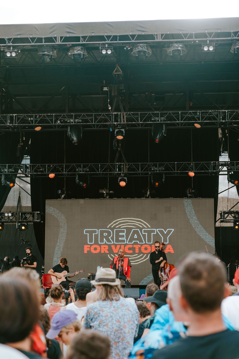 A band performs on stage with 'Treaty for Victoria' text displayed on a screen behind them.