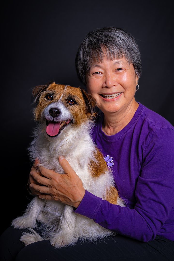 A happy brown and white terrier Dr. Watson poses with their companion Nancy against a dark backdrop.