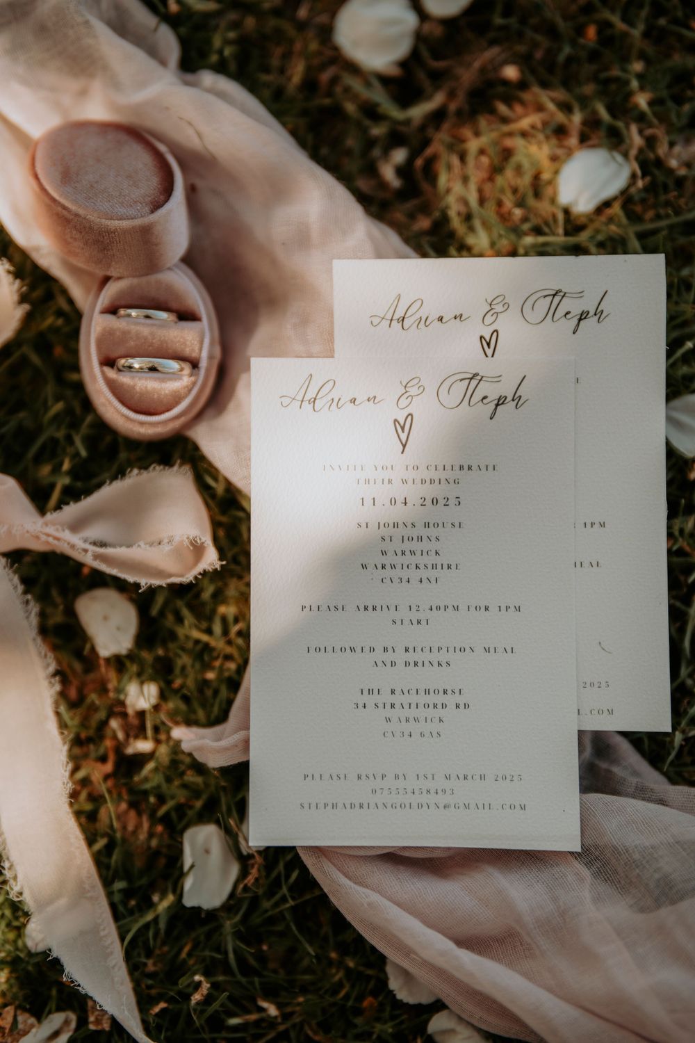 Elegant wedding program with rose gold lettering displayed with rings on soft fabric and white petals on the ground.