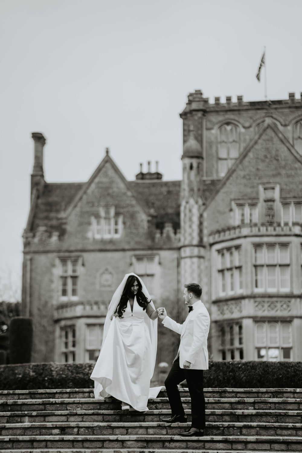 A couple shares a romantic moment on stone steps with a gothic castle-like building in the background.