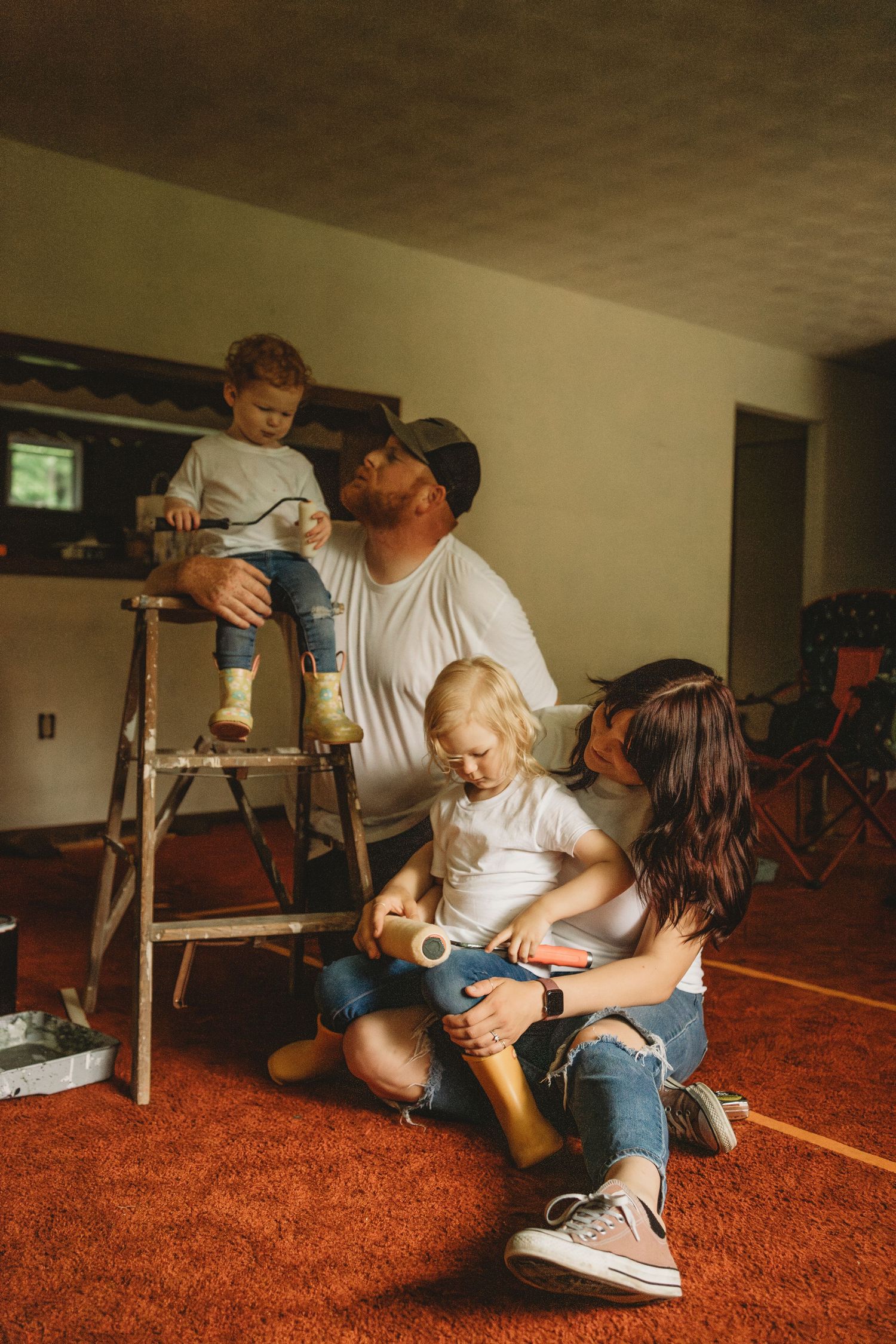 Family spending time together during home renovation with step ladder and orange carpet.