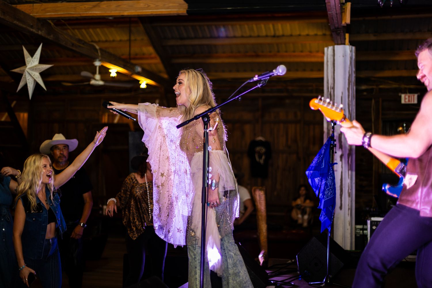 Band performs on stage in a dimly lit venue with crowd silhouettes visible.