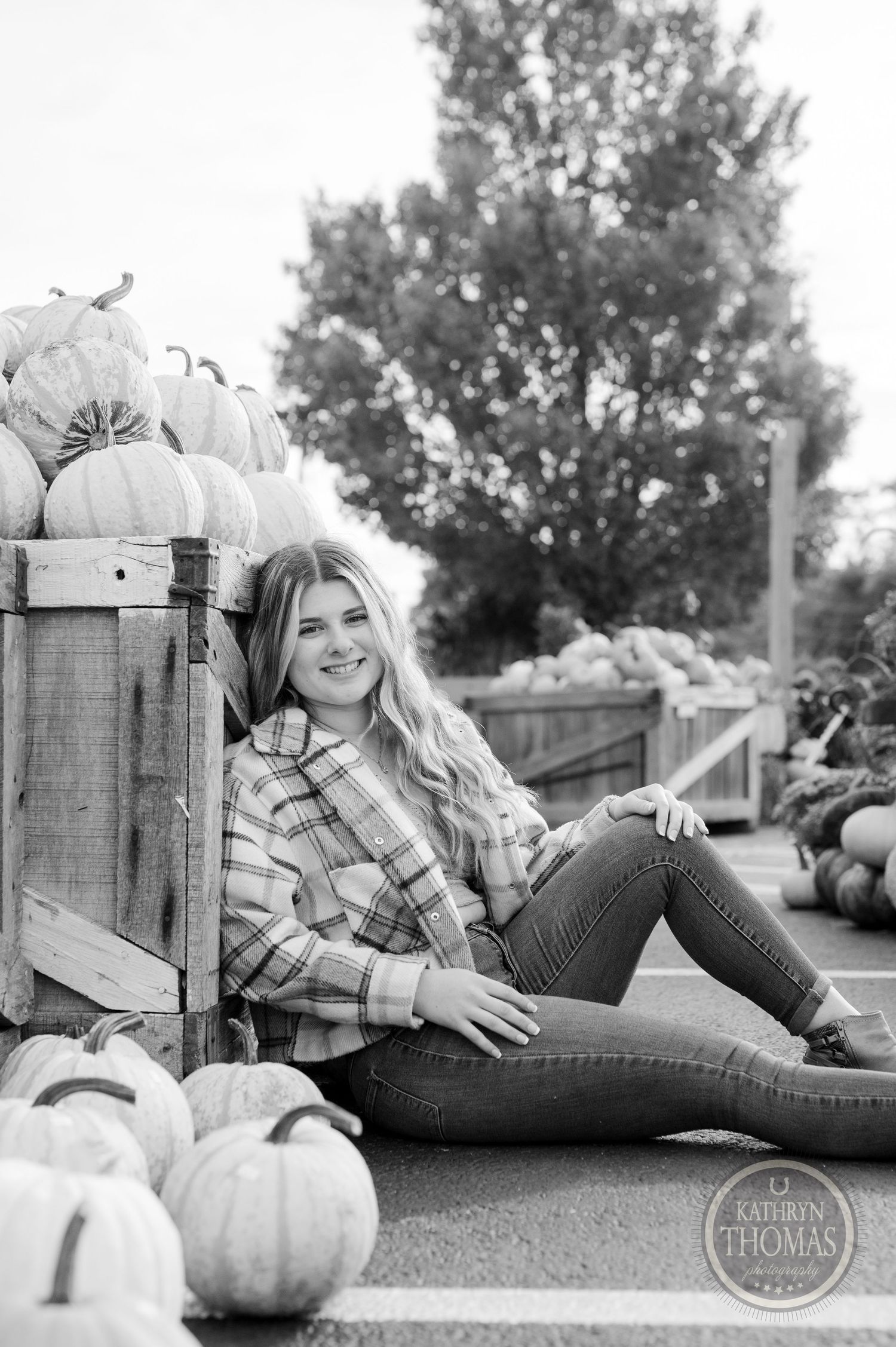Black and white portrait of someone reclining against wooden crates filled with pumpkins.