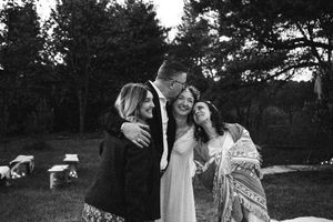 A joyful group embraces and laughs together at an outdoor gathering in black and white.