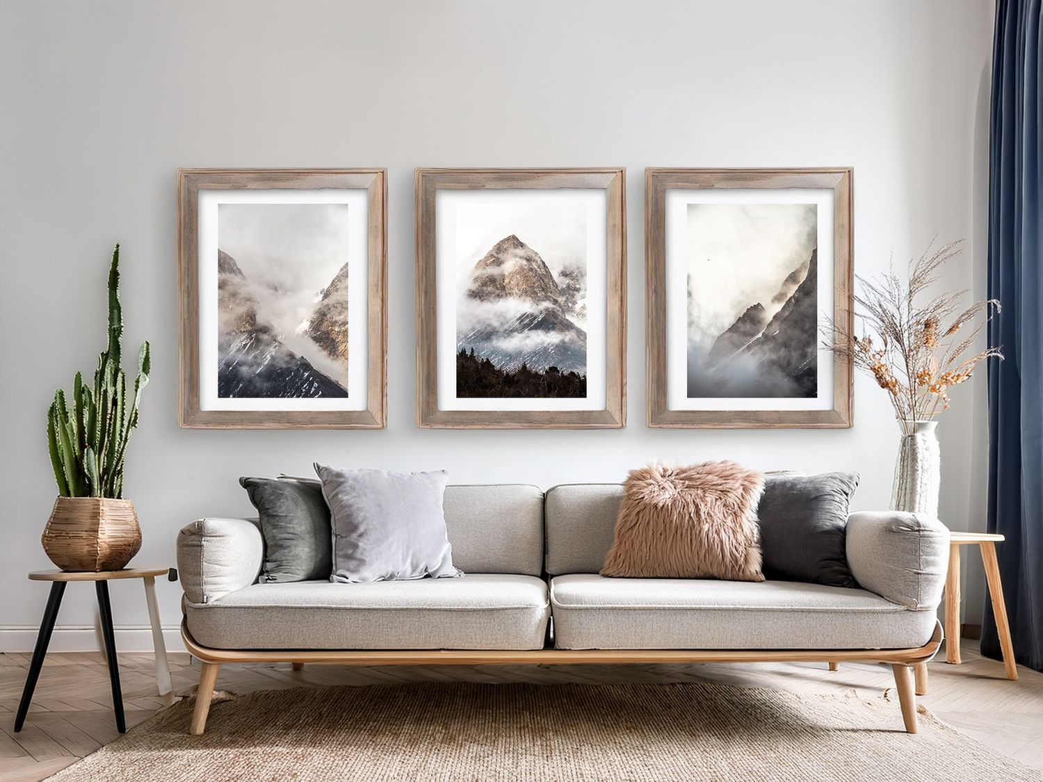 Modern living room with three framed mountain prints above a gray sofa and decorative potted plants.