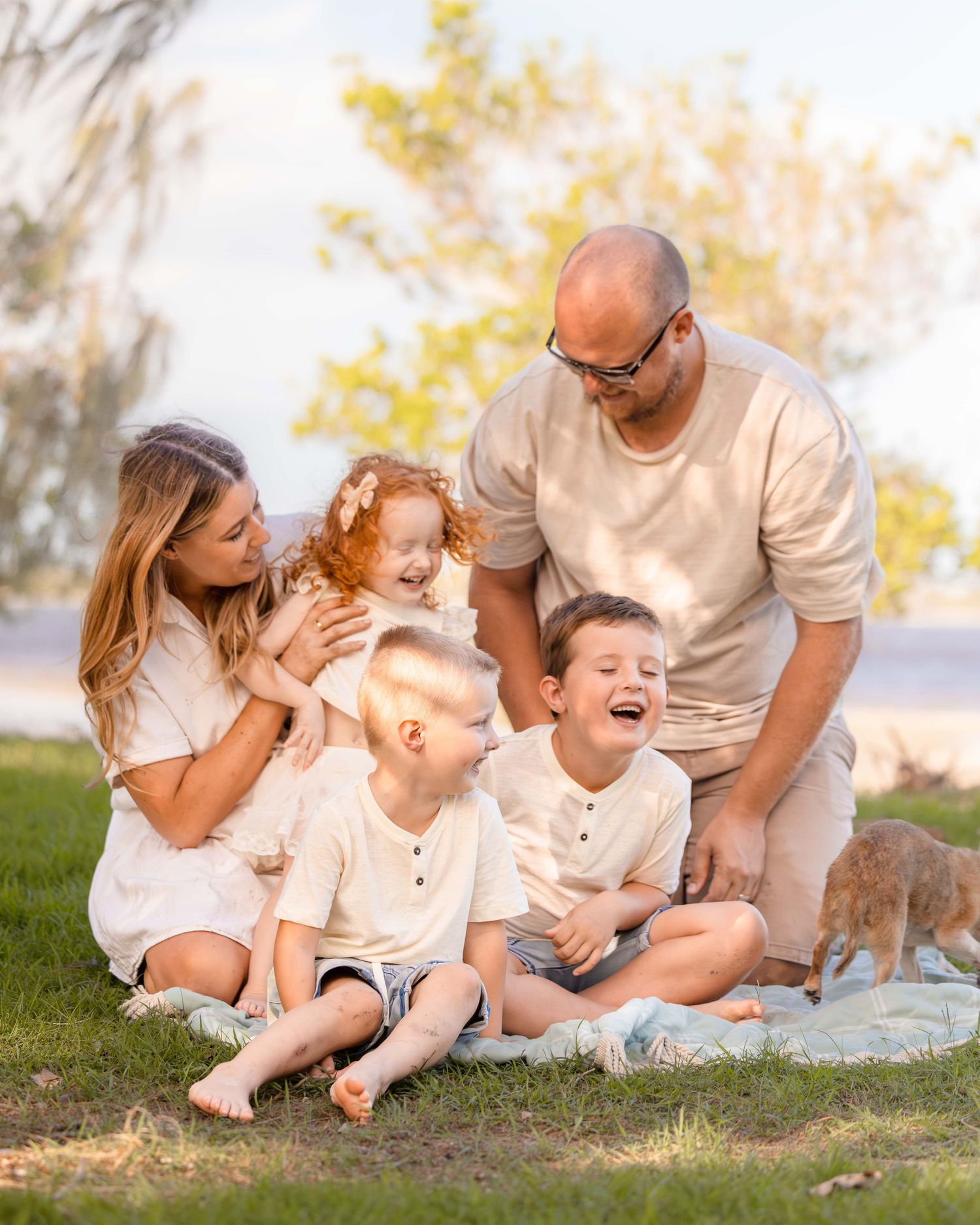 Gorgeous family of 6 on a blanket on the beach being lit by the afternoon sun. Together they smile and share a moment of joy as a family.