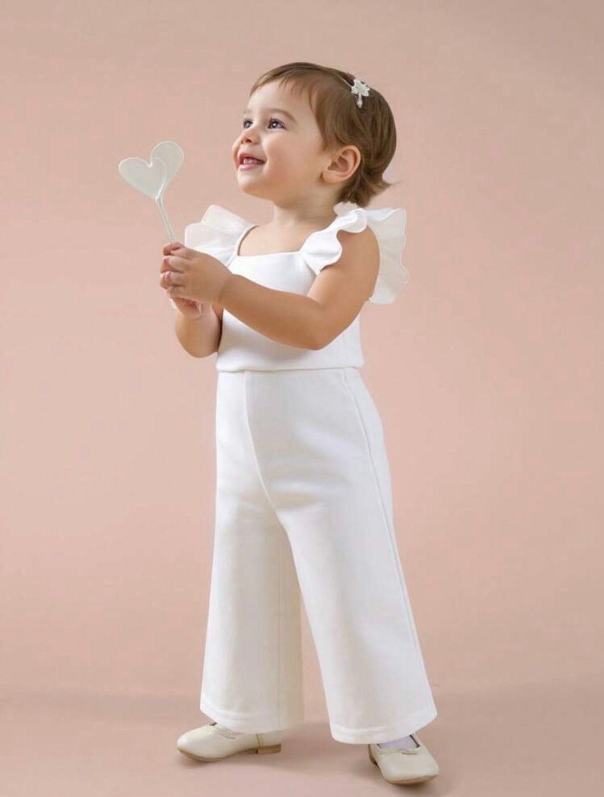 Baby wearing white outfit playing with butterfly decorations against pink background.